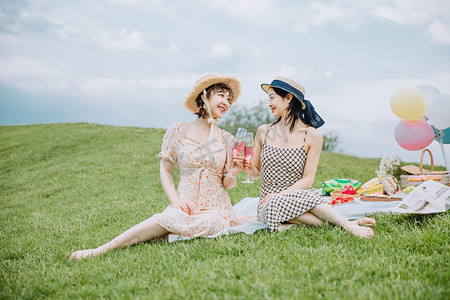郊游野餐白天坐在草地上的闺蜜草地喝酒聊天摄影图配图