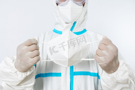 防护服摄影照片_防疫疫情医生棚拍穿着防护服拿口罩动作摄影图配图