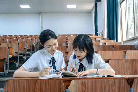 桌椅摄影照片_人像白天两个女大学生教室认真学习摄影图配图