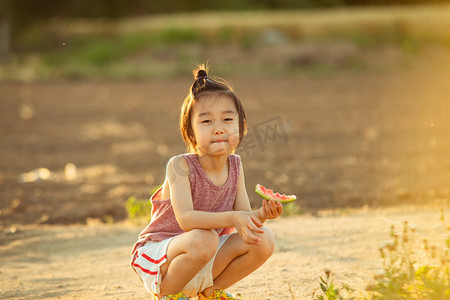夏日儿童人像夕阳可爱小男生田地旁抿嘴吃西瓜摄影图配图