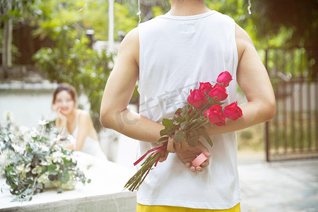 520表白日粉色摄影照片_情人节白天一对情侣户外把玫瑰花藏在身后摄影图配图