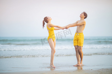 爱情情人节白天一对情侣户外沙滩手拉手转圈摄影图配图