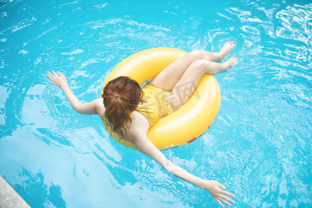 夏天泳池摄影照片_夏天游泳白天坐在游泳圈里的美女泳池滑水摄影图配图