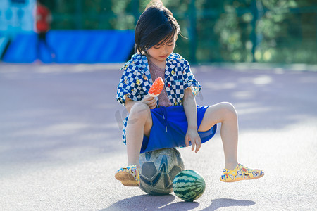 夏日儿童人像白天长发小男生操场坐足球玩西瓜吃冰棍摄影图配图