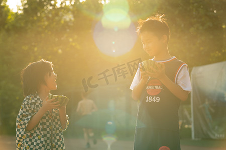 西瓜摄影照片_两人夏日人像白天兄弟二人逆光下抱着西瓜开心对视摄影图配图