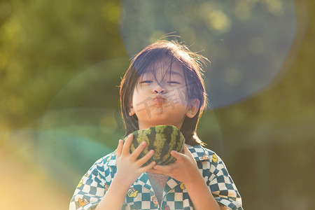 夏季大暑摄影照片_夏日儿童人像白天长发小男孩阳光下可爱吃西瓜摄影图配图