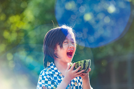 夏日儿童人像白天长发小男生阳光下抱着西瓜开心的大笑摄影图配图
