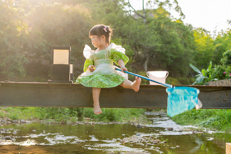 夏天小溪摄影照片_夕阳下的女孩傍晚儿童户外捞鱼摄影图配图