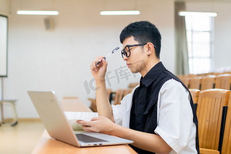 暖色调电脑壁纸摄影照片_教室里使用笔记本电脑思考的男大学生