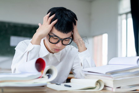 眼镜摄影照片_在教室里自习复习疲惫的戴眼镜男同学