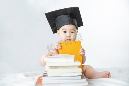 婴儿启蒙教育白天书堆里的男婴室内拿着书摄影图配图