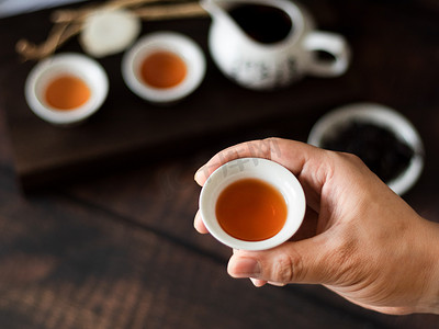绿茶茶叶摄影照片_喝茶手拿茶杯白天茶具茶室喝茶摄影图配图