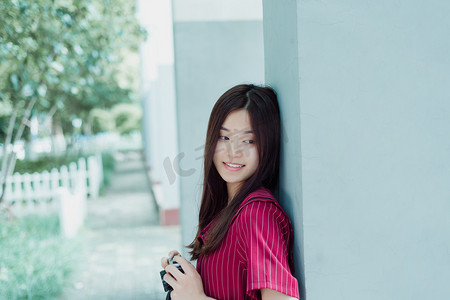夏日文艺人像白天一个女生倚在墙上拿着相机开心的笑摄影图配图