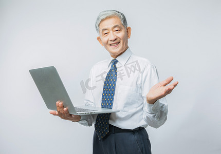 晚年生活摄影照片_老年生活白天老年人室内拿着电脑欢迎手势摄影图配图