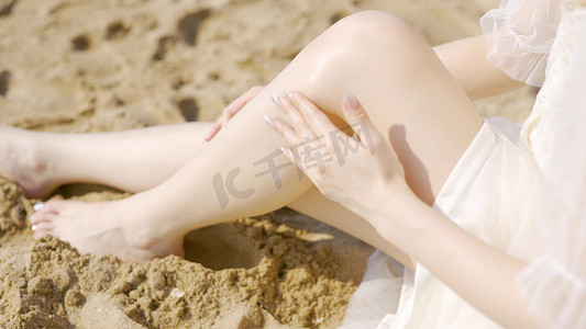 摄影照片_美女沙滩阳光涂抹防晒油腿部特写广告宣传素材