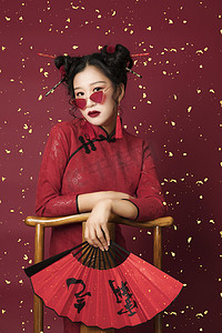 国潮摄影照片_国潮复兴白天穿着红色旗袍的美女室内拿着中式扇子摄影图配图