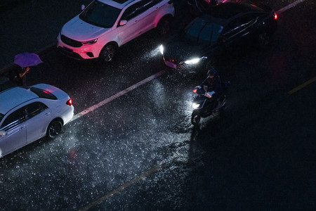 防汛预警摄影照片_暴雨出行傍晚汽车和电动车马路出行交通摄影图配图