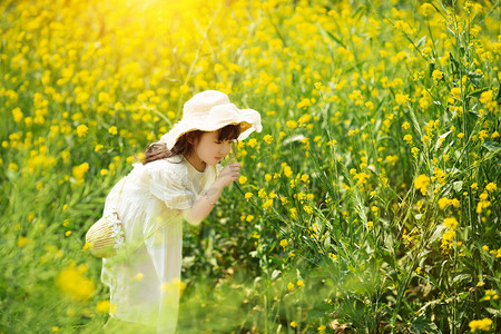 治愈摄影照片_唯美的小女孩低头闻油菜花治愈画面摄影图配图