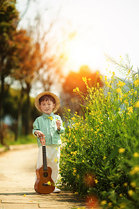 小男孩手拿吉他站在水泥地上春游摄影图配图