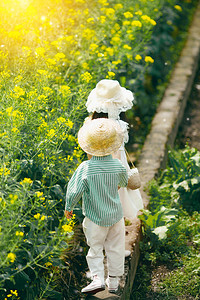 姐姐拉着弟弟的手走在油菜花田埂上摄影图配图