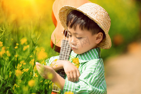 小男手拿吉他孩在油菜花田玩耍摄影图配图