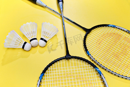 黄色背景上的运动器械羽毛球拍和球静物特写摄影图配图