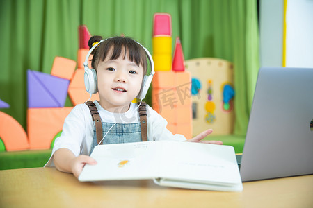 可爱幼儿园摄影照片_儿童教育白天可爱女孩教室戴着耳机上课摄影图配图