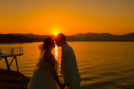 夕阳婚纱照剪影两个人户外亲吻摄影图配图