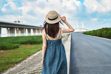 公路旁夏日晴天女生背面蓝天白云散步摄影图配图