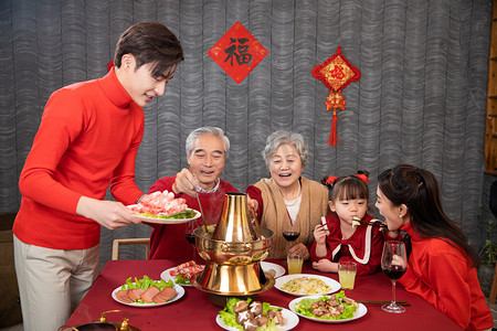 除夕孩子摄影照片_年夜饭吃火锅年轻妈妈夹菜喂孩子摄影图配图