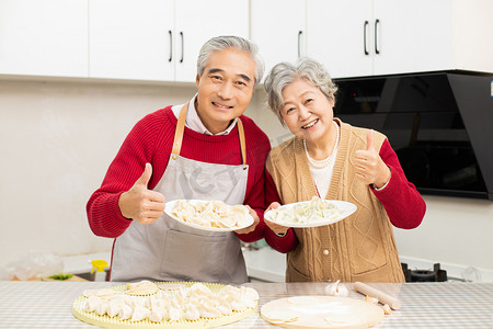 厨房里手端着饺子点赞的老年夫妻摄影图配图