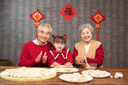 除夕爷爷奶奶教小女孩包饺子摄影图配图