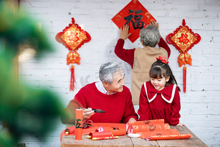 春节春联摄影照片_大年三十爷爷教小女孩写春联奶奶贴春联摄影图配图