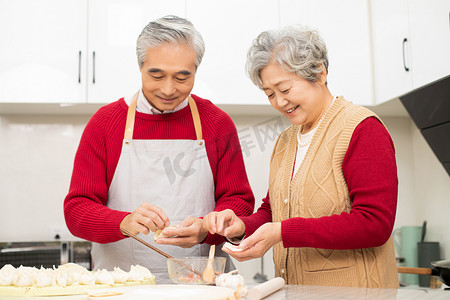 春节习俗大年初三摄影照片_除夕在厨房准备包饺子的老年夫妻摄影图配图