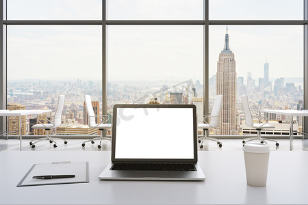 Front view of the workplace in a modern panoramic office in New York. White tables and white chairs. A laptop with a white display, notepad and a coffee cup are on the table. 3D rendering.