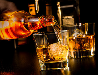 酒吧摄影照片_酒保倒在威士忌玻璃和瓶威士忌