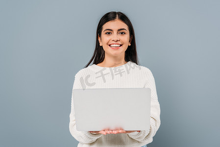 穿着白色毛衣，手里拿着灰色笔记本电脑的漂亮的黑发姑娘笑着