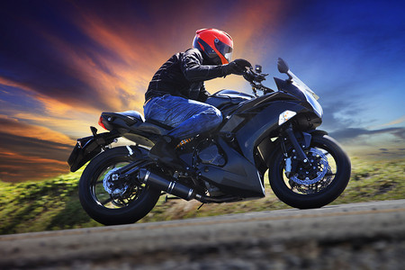 摩托车背景摄影照片_沥青国家道路上骑摩托车的年轻男子