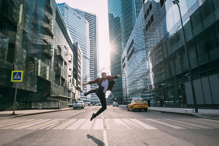欧美建筑摄影照片_一个男人从市中心的一个人行横道上跳过.在一座大城市的摩天大楼的背景下，一个年轻时髦的小伙子在日落前摆姿势