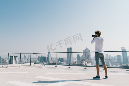 年轻白人白人男子在阳光明媚的一天, 在屋顶上拍摄城市景观照片。摄影嗜好、小工具技术或休闲活动概念。蓝天上的复制空间