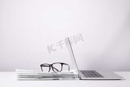 laptop and eyeglasses on heap of newspapers, on white