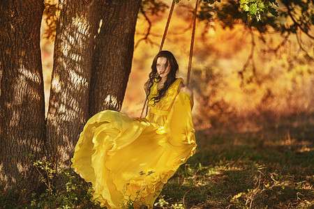 美丽的女孩在一件黄色的连衣裙，骑在秋千上