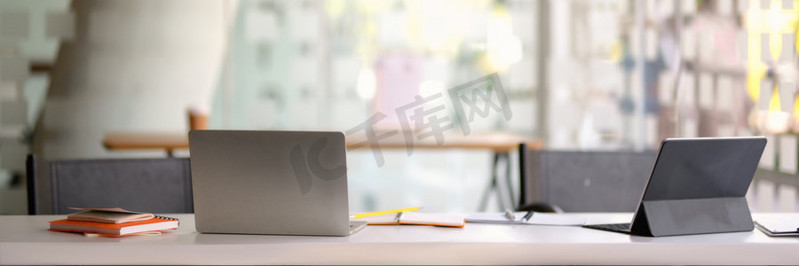 玻璃幕墙办公室白色桌子上带有笔记本电脑和平板电脑的便携式工作空间的裁剪照片