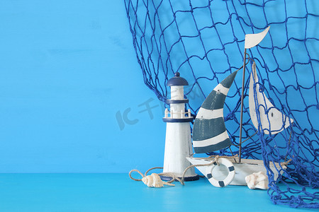 贝壳摄影照片_航海概念以白色装饰风帆小船、灯塔、海贝壳和鱼网在蓝色木桌和背景.