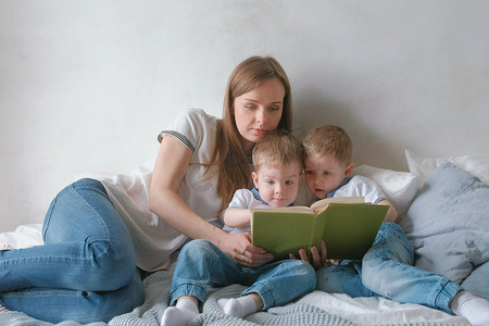家里的妈妈和两个双胞胎兄弟在床上看书。家庭阅读时间.
