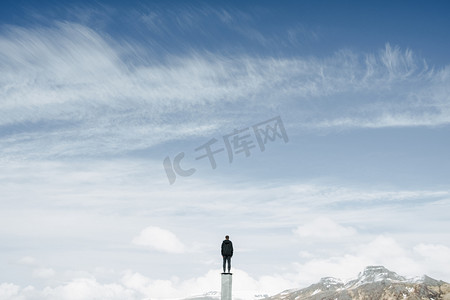 创意会议背景摄影照片_男人独自站在柱子上看着天空和山脉的寂寞和简约的概念, 复制空间 
