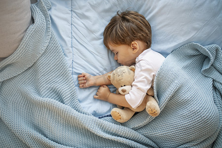 喜欢摄影照片_男婴与泰迪熊睡在一起的照片。他最喜欢的午睡点。可爱的男孩睡在床上与玩具后。男孩睡在床上与泰迪熊。懒虫