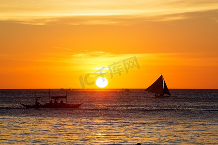 在日落时在热带海洋上的帆船。剪影照片.