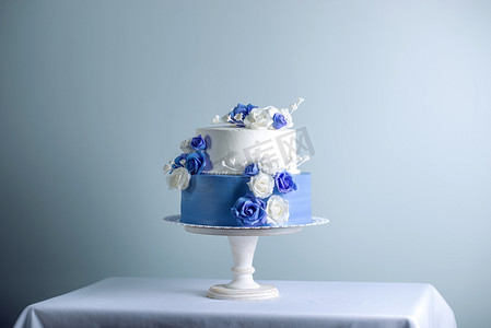 美丽的两个分层的白色和蓝色婚礼蛋糕装饰花糖玫瑰。优雅假日甜点概念
