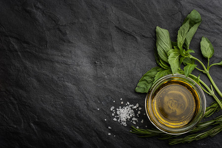 黑色石头摄影照片_Olive oil  with different greens on the right side of the black stone table